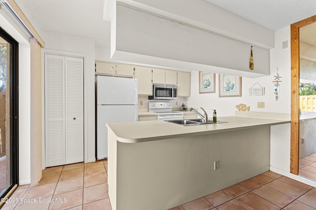 kitchen with light tile patterned floors, a peninsula, white appliances, and a sink