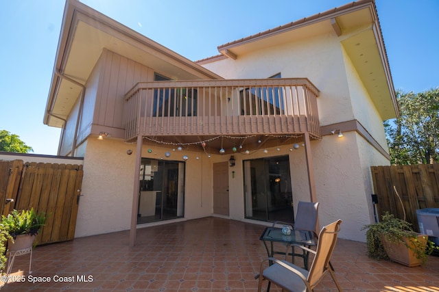 back of house featuring stucco siding, a patio, a balcony, and fence