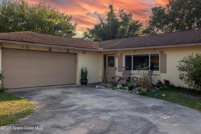 ranch-style home with a garage, roof with shingles, driveway, and stucco siding