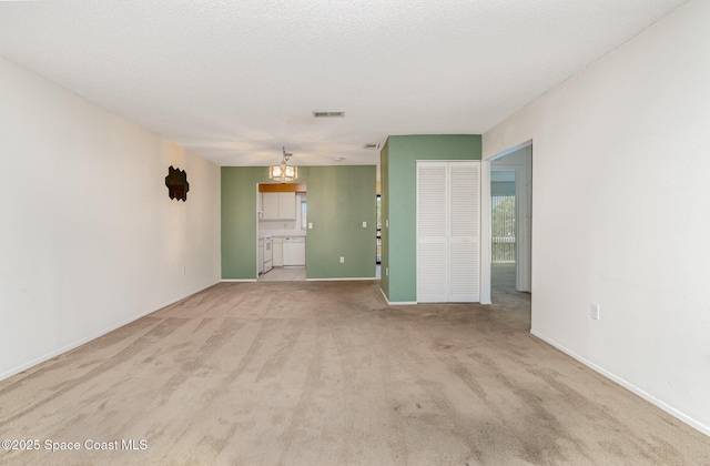 spare room with a chandelier, a textured ceiling, light carpet, visible vents, and baseboards