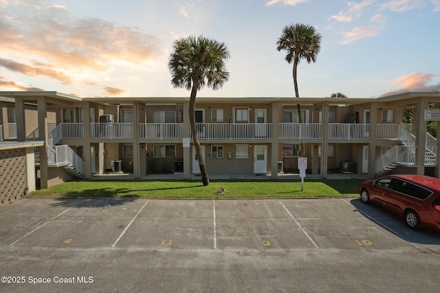 property at dusk with stairs, uncovered parking, and central AC unit