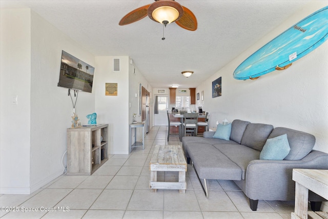 living area featuring light tile patterned floors, visible vents, a ceiling fan, a textured ceiling, and baseboards