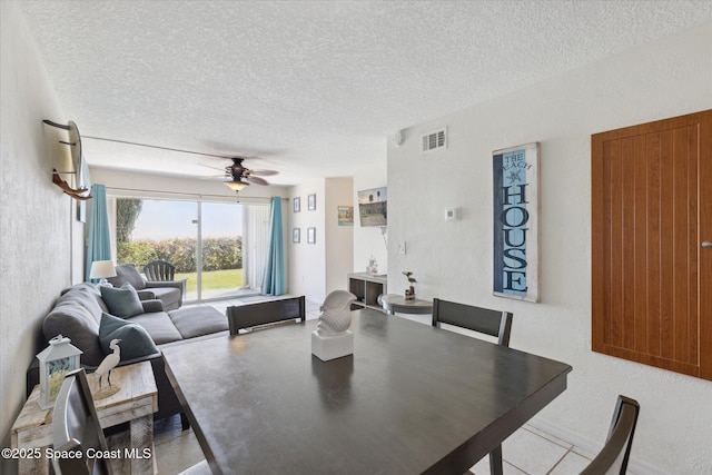 dining room with a ceiling fan, visible vents, a textured wall, and a textured ceiling