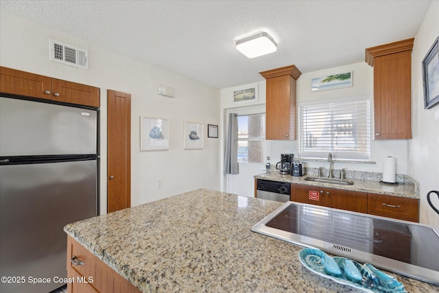 kitchen with stainless steel appliances, a sink, visible vents, brown cabinets, and light stone countertops