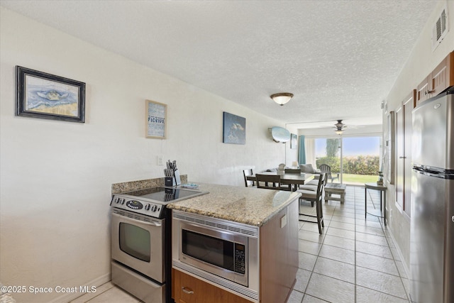 kitchen with light tile patterned floors, visible vents, appliances with stainless steel finishes, brown cabinetry, and a textured ceiling