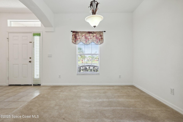 foyer entrance featuring arched walkways, light colored carpet, baseboards, and light tile patterned flooring