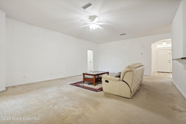 living area with visible vents, light carpet, a ceiling fan, arched walkways, and baseboards