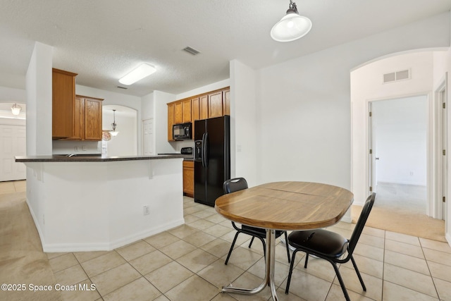 kitchen with visible vents, brown cabinets, black appliances, dark countertops, and arched walkways