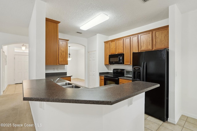 kitchen with a peninsula, arched walkways, a sink, black appliances, and dark countertops