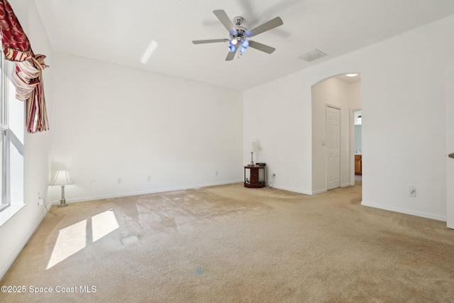 empty room featuring visible vents, baseboards, ceiling fan, light colored carpet, and arched walkways