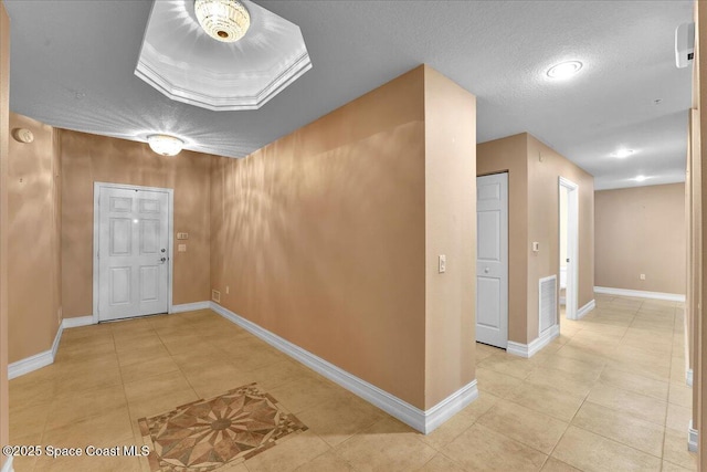 hall featuring baseboards, visible vents, a textured ceiling, and light tile patterned flooring
