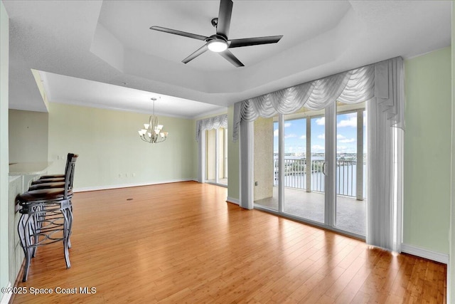 interior space featuring baseboards, a raised ceiling, wood finished floors, a water view, and ceiling fan with notable chandelier