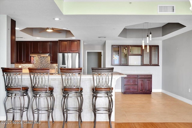 kitchen featuring visible vents, stainless steel fridge, a raised ceiling, and glass insert cabinets