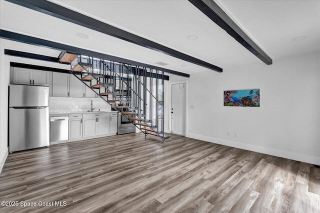 unfurnished living room featuring wood finished floors, beam ceiling, baseboards, and stairs