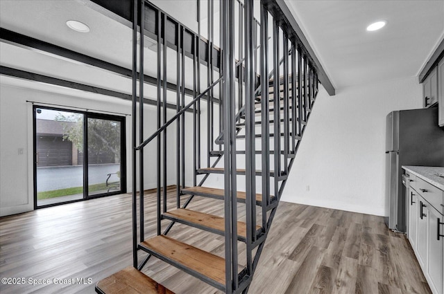 stairway with recessed lighting, beam ceiling, baseboards, and wood finished floors