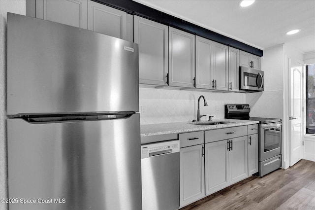 kitchen with gray cabinetry, decorative backsplash, appliances with stainless steel finishes, light wood-style floors, and a sink