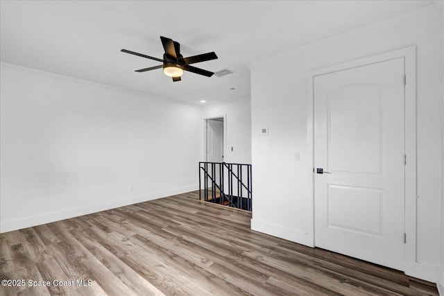 spare room with crown molding, visible vents, a ceiling fan, wood finished floors, and baseboards