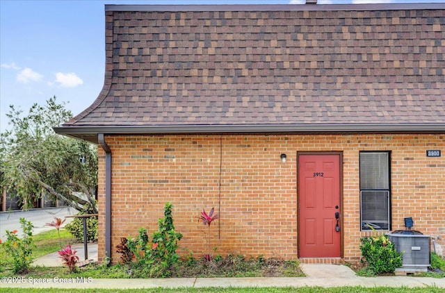 view of front of house with brick siding, roof with shingles, and cooling unit