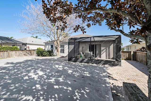 view of front of house with stucco siding, a fenced backyard, glass enclosure, and a patio