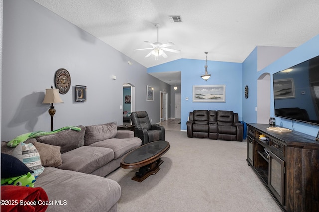 living area with light carpet, visible vents, arched walkways, lofted ceiling, and a textured ceiling