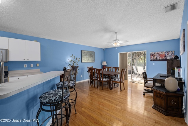 dining area with a textured ceiling, a ceiling fan, visible vents, baseboards, and light wood finished floors