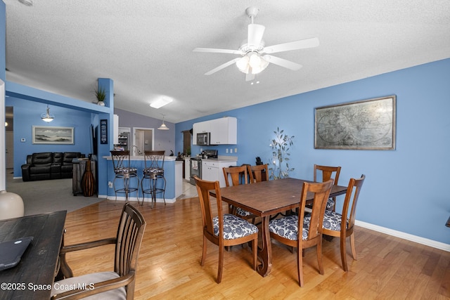 dining space featuring baseboards, a ceiling fan, vaulted ceiling, a textured ceiling, and light wood-style floors