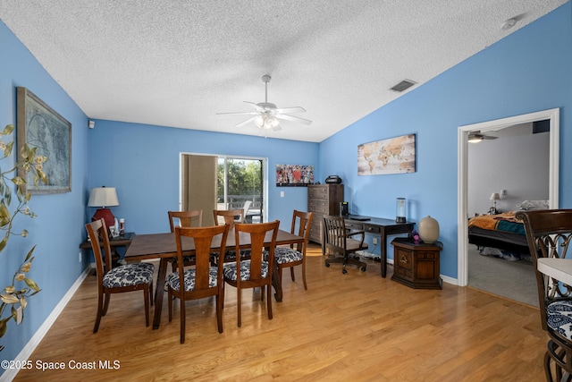 dining area featuring visible vents, a ceiling fan, light wood-style floors, vaulted ceiling, and a textured ceiling