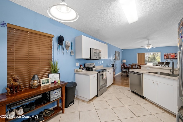 kitchen with light tile patterned floors, light countertops, appliances with stainless steel finishes, white cabinets, and a sink