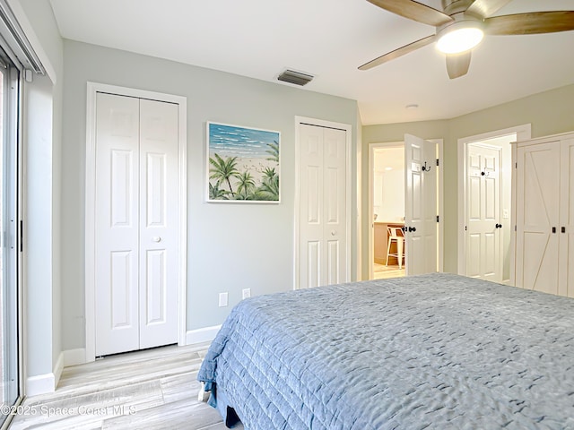 bedroom featuring light wood finished floors, baseboards, visible vents, a ceiling fan, and two closets