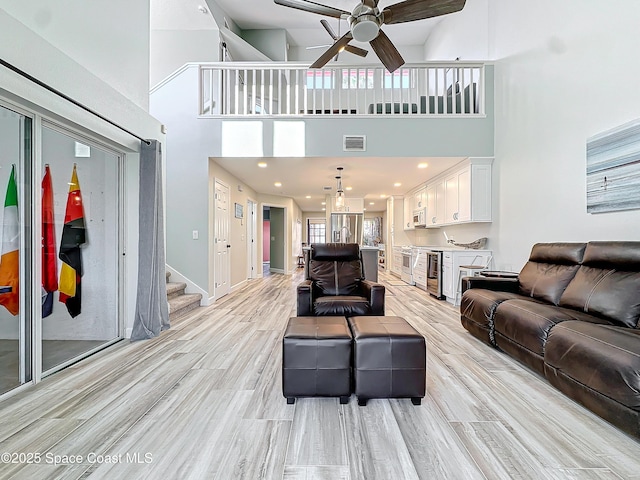 living room with ceiling fan, visible vents, baseboards, light wood-style floors, and stairway