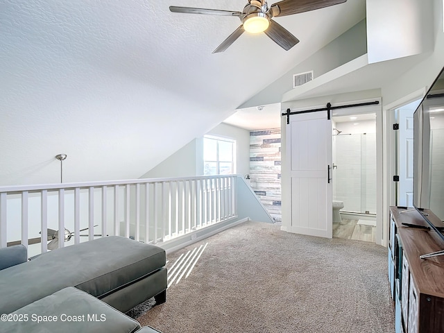 sitting room with lofted ceiling, a textured ceiling, a barn door, a ceiling fan, and carpet