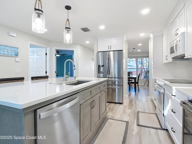 kitchen with stainless steel appliances, light countertops, visible vents, a kitchen island with sink, and a sink