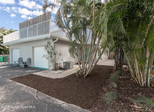 view of home's exterior with concrete driveway, a balcony, central air condition unit, and stucco siding