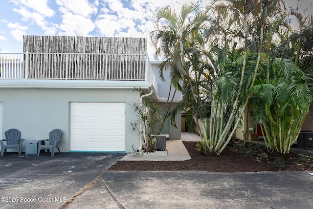 view of front facade with a balcony, central air condition unit, a garage, concrete driveway, and stucco siding