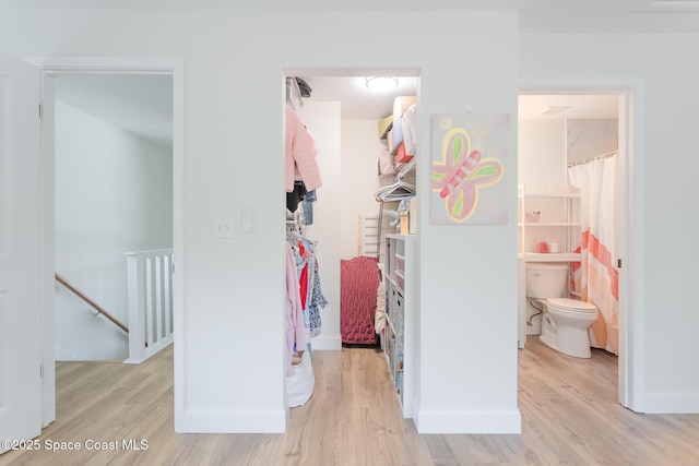 interior space with a spacious closet, light wood-type flooring, ensuite bath, and baseboards