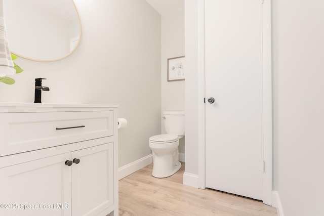 half bathroom with toilet, baseboards, wood finished floors, and vanity