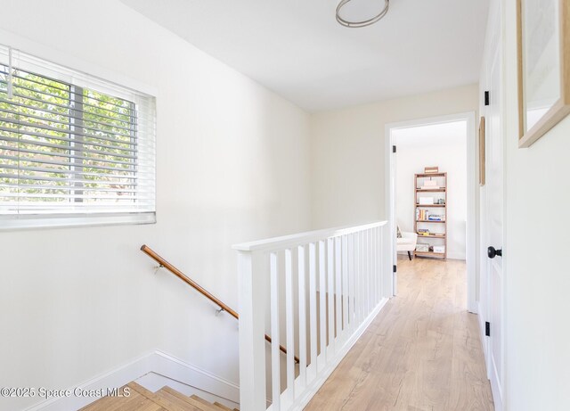 corridor with light wood-type flooring, baseboards, and an upstairs landing