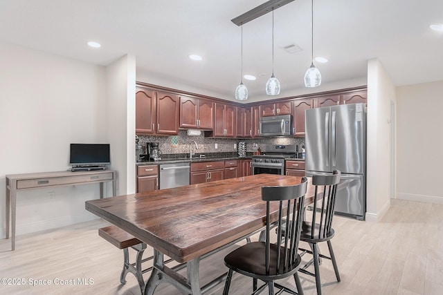 kitchen with stainless steel appliances, hanging light fixtures, light wood-type flooring, tasteful backsplash, and dark countertops