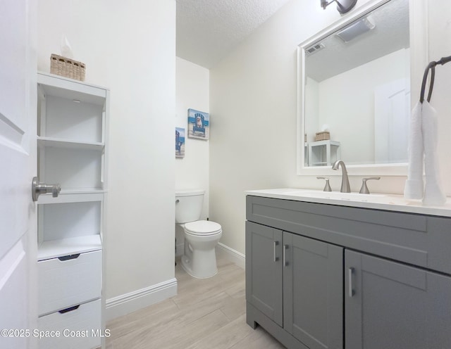 half bath featuring visible vents, vanity, a textured ceiling, wood finished floors, and baseboards