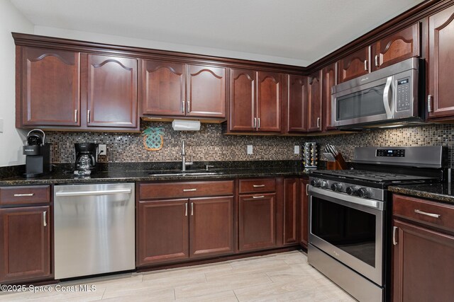 kitchen with stainless steel appliances, a sink, decorative backsplash, and dark stone countertops