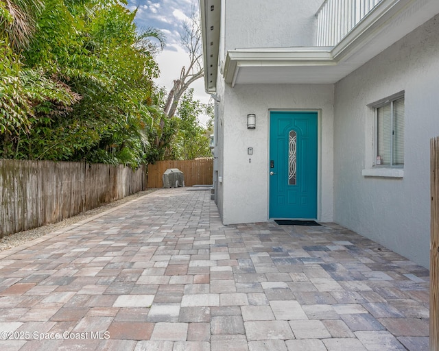 entrance to property with fence, a patio, and stucco siding