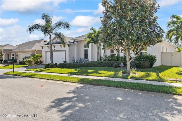 view of front of property featuring a garage, fence, driveway, stucco siding, and a front yard