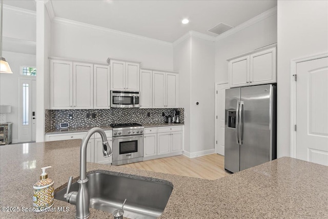 kitchen with appliances with stainless steel finishes, backsplash, a sink, and ornamental molding