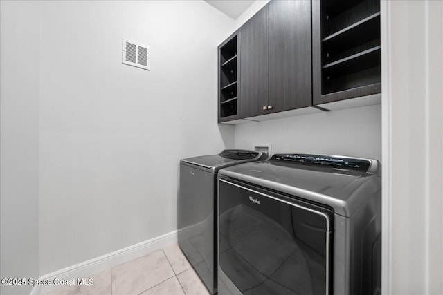 washroom with cabinet space, visible vents, washing machine and dryer, light tile patterned flooring, and baseboards