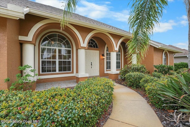 doorway to property featuring roof with shingles and stucco siding