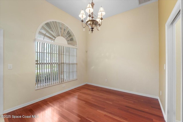 empty room with a notable chandelier, wood finished floors, visible vents, and baseboards