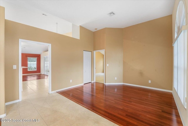 spare room with a towering ceiling, light wood finished floors, baseboards, and visible vents