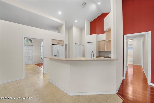 kitchen with high vaulted ceiling, visible vents, baseboards, light countertops, and white fridge with ice dispenser