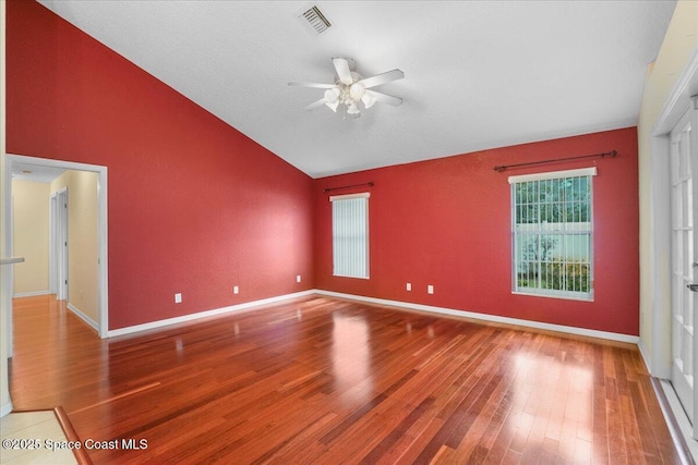 empty room with lofted ceiling, a ceiling fan, visible vents, and wood finished floors