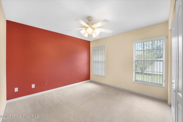 empty room with a textured ceiling, ceiling fan, baseboards, and light colored carpet